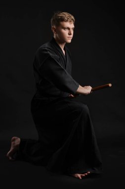 Geleneksel Japon kimonosu giymiş Kendo gurusu Shinai bambu kılıcıyla siyah bir stüdyoda dövüş sanatları eğitimi alıyor..