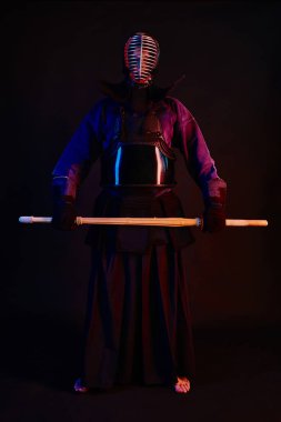 Yakın çekim, Kendo dövüşçüsü zırh giyiyor, geleneksel kimono giyiyor, miğfer takıyor shinai bambu kılıcıyla dövüş sanatları yapıyor, siyah arka plan.