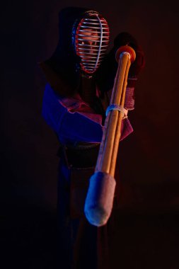 Yakın çekim, Kendo dövüşçüsü zırh giyiyor, geleneksel kimono giyiyor, miğfer takıyor shinai bambu kılıcıyla dövüş sanatları yapıyor, siyah arka plan.