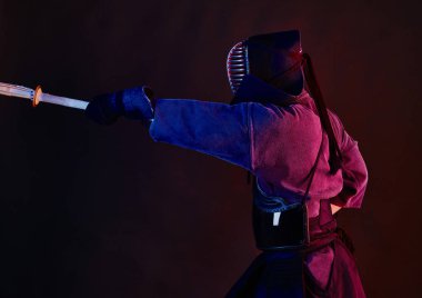 Yakın çekim, Kendo dövüşçüsü zırh giyiyor, geleneksel kimono giyiyor, miğfer takıyor shinai bambu kılıcıyla dövüş sanatları yapıyor, siyah arka plan.