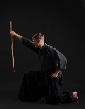Geleneksel Japon kimonosu giymiş Kendo gurusu Shinai bambu kılıcıyla siyah bir stüdyoda dövüş sanatları eğitimi alıyor..