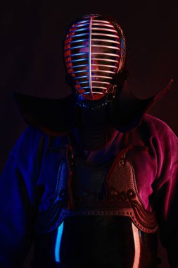 Yakın çekim, Kendo dövüşçüsü zırh giyiyor, geleneksel kimono giyiyor, miğfer takıyor shinai bambu kılıcıyla dövüş sanatları yapıyor, siyah arka plan.