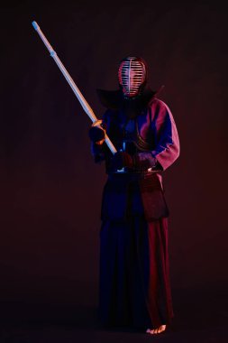 Yakın çekim, Kendo dövüşçüsü zırh giyiyor, geleneksel kimono giyiyor, miğfer takıyor shinai bambu kılıcıyla dövüş sanatları yapıyor, siyah arka plan.