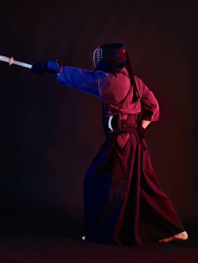 Yakın çekim, Kendo dövüşçüsü zırh giyiyor, geleneksel kimono giyiyor, miğfer takıyor shinai bambu kılıcıyla dövüş sanatları yapıyor, siyah arka plan.