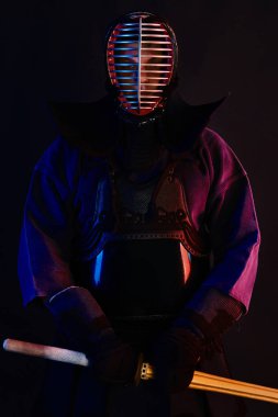 Yakın çekim, Kendo dövüşçüsü zırh giyiyor, geleneksel kimono giyiyor, miğfer takıyor shinai bambu kılıcıyla dövüş sanatları yapıyor, siyah arka plan.