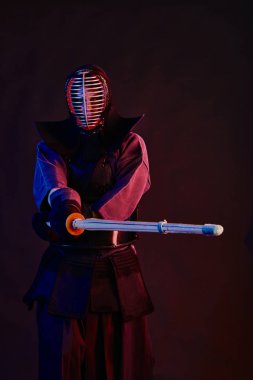 Yakın çekim, Kendo dövüşçüsü zırh giyiyor, geleneksel kimono giyiyor, miğfer takıyor shinai bambu kılıcıyla dövüş sanatları yapıyor, siyah arka plan.