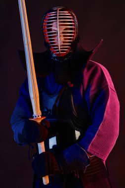 Yakın çekim, Kendo dövüşçüsü zırh giyiyor, geleneksel kimono giyiyor, miğfer takıyor shinai bambu kılıcıyla dövüş sanatları yapıyor, siyah arka plan.