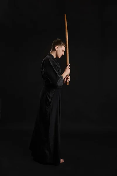 Kendo guru vestindo em um kimono japonês tradicional está praticando arte marcial com a espada de bambu de xadrez contra um fundo de estúdio preto. — Fotografia de Stock