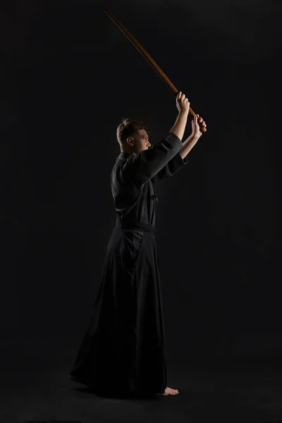 Kendo guru bär i en traditionell japansk kimono tränar kampsport med shinai bambu svärd mot en svart studio bakgrund. — Stockfoto