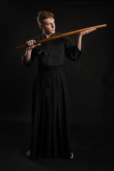 Kendo guru wearing in a traditional japanese kimono is practicing martial art with the shinai bamboo sword against a black studio background. — Stock Photo, Image