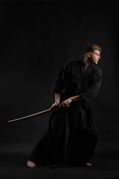 Кендо-гуру в традиционном кимоно отрабатывает мартиальное искусство с синайским мечом на черном студийном фоне.