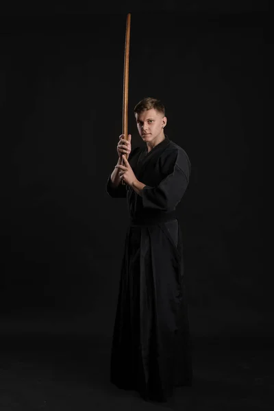 Kendo guru wearing in a traditional japanese kimono is practicing martial art with the shinai bamboo sword against a black studio background. — Stock Photo, Image