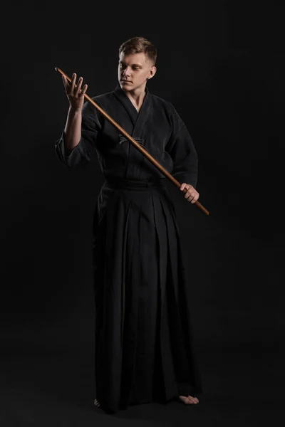 Kendo guru φορώντας ένα παραδοσιακό ιαπωνικό κιμονό ασκεί πολεμικές τέχνες με το σπαθί μπαμπού shinai σε μαύρο φόντο στούντιο. — Φωτογραφία Αρχείου