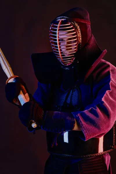 Yakın çekim, Kendo dövüşçüsü zırh giyiyor, geleneksel kimono giyiyor, miğfer takıyor shinai bambu kılıcıyla dövüş sanatları yapıyor, siyah arka plan.