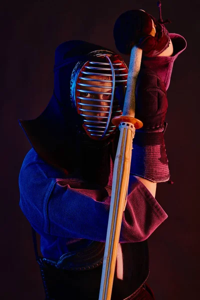 Gros plan, Combattant Kendo vêtu d'une armure, kimono traditionnel, casque pratiquant l'art martial avec épée de bambou shinai, fond noir . — Photo