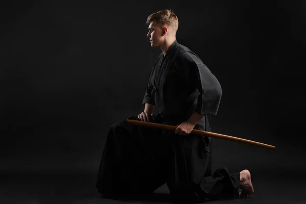 Le gourou kendo portant un kimono japonais traditionnel s'exerce à l'art martial avec l "épée de bambou shinai sur fond de studio noir.. — Photo