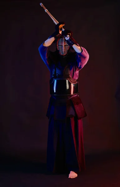 Gros plan, Combattant Kendo vêtu d'une armure, kimono traditionnel, casque pratiquant l'art martial avec épée de bambou shinai, fond noir . — Photo