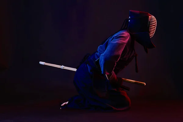 Зблизька стрілянина, боєць Кендо, одягнений в обладунки, традиційний кімоно, шолом практикує бойове мистецтво з шинайським бамбуковим мечем, чорний фон. — стокове фото