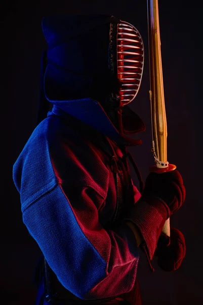 Yakın çekim, Kendo dövüşçüsü zırh giyiyor, geleneksel kimono giyiyor, miğfer takıyor shinai bambu kılıcıyla dövüş sanatları yapıyor, siyah arka plan.