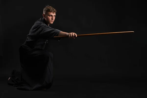 Kendo guru wearing in a traditional japanese kimono is practicing martial art with the shinai bamboo sword against a black studio background. Royalty Free Stock Photos