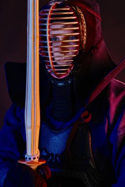 Yakın çekim, Kendo dövüşçüsü zırh giyiyor, geleneksel kimono giyiyor, miğfer takıyor shinai bambu kılıcıyla dövüş sanatları yapıyor, siyah arka plan.