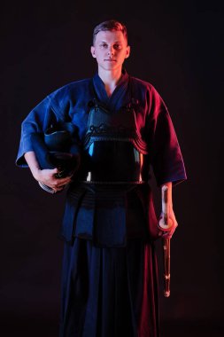 Geleneksel kimono, siyah arka planda poz verirken kaskını ve shinai bambu kılıcını tutuyor. Kapat..