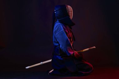 Yakın çekim, Kendo dövüşçüsü zırh giyiyor, geleneksel kimono giyiyor, miğfer takıyor shinai bambu kılıcıyla dövüş sanatları yapıyor, siyah arka plan.