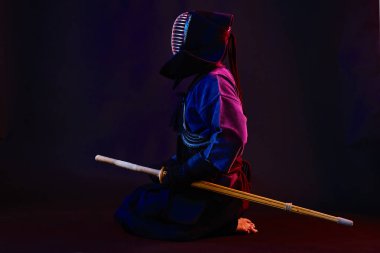 Yakın çekim, Kendo dövüşçüsü zırh giyiyor, geleneksel kimono giyiyor, miğfer takıyor shinai bambu kılıcıyla dövüş sanatları yapıyor, siyah arka plan.