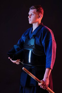 Geleneksel kimono, siyah arka planda poz verirken kaskını ve shinai bambu kılıcını tutuyor. Kapat..