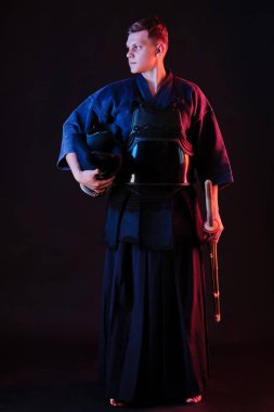 Geleneksel kimono, siyah arka planda poz verirken kaskını ve shinai bambu kılıcını tutuyor. Kapat..