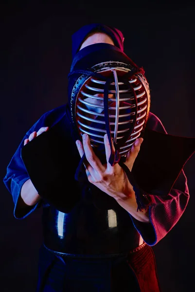 Close up shot, Kendo fighter wearing in an armor and traditional kimono is tying the lacing on his helmet standing against a black background. — Stock Photo, Image