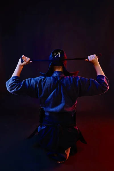 Cerrado el tiro, el luchador de Kendo con armadura y kimono tradicional está atando la laca de su casco de pie contra un fondo negro.. —  Fotos de Stock