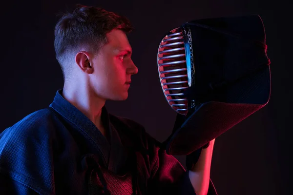 Närbild skott, Kendo fighter bär i en rustning, traditionell kimono tittar på sin hjälm när du står mot en svart studio bakgrund. — Stockfoto