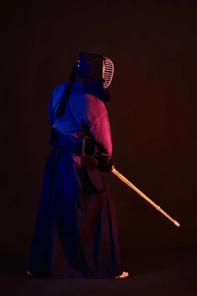 Närbild skott, Kendo fighter bär i en rustning, traditionell kimono, hjälm öva kampsport med shinai bambu svärd, svart bakgrund. — Stockfoto