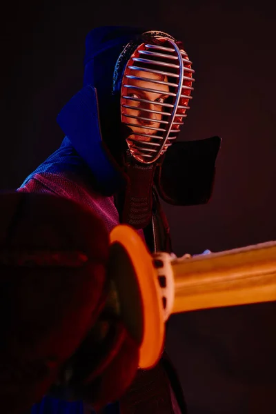 Närbild skott, Kendo fighter bär i en rustning, traditionell kimono, hjälm öva kampsport med shinai bambu svärd, svart bakgrund. — Stockfoto