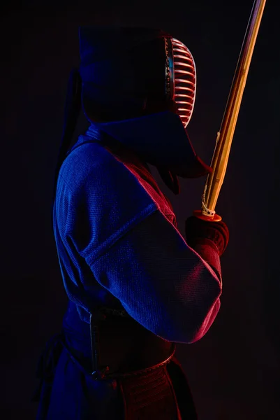 Close-up schot, Kendo vechter dragen in een harnas, traditionele kimono, helm beoefenen van krijgskunst met shinai bamboe zwaard, zwarte achtergrond. — Stockfoto