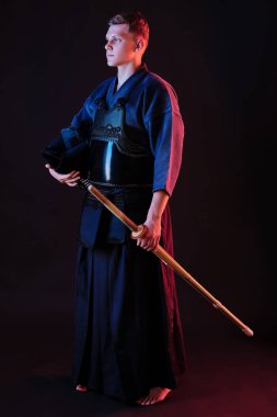 Geleneksel kimono, siyah arka planda poz verirken kaskını ve shinai bambu kılıcını tutuyor. Kapat..
