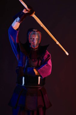 Yakın çekim, Kendo dövüşçüsü zırh giyiyor, geleneksel kimono giyiyor, miğfer takıyor shinai bambu kılıcıyla dövüş sanatları yapıyor, siyah arka plan.