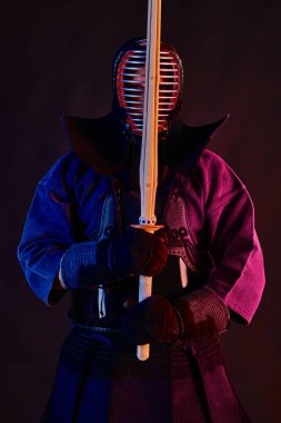 Yakın çekim, Kendo dövüşçüsü zırh giyiyor, geleneksel kimono giyiyor, miğfer takıyor shinai bambu kılıcıyla dövüş sanatları yapıyor, siyah arka plan.