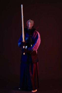 Yakın çekim, Kendo dövüşçüsü zırh giyiyor, geleneksel kimono giyiyor, miğfer takıyor shinai bambu kılıcıyla dövüş sanatları yapıyor, siyah arka plan.
