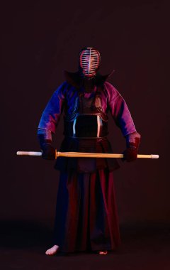 Yakın çekim, Kendo dövüşçüsü zırh giyiyor, geleneksel kimono giyiyor, miğfer takıyor shinai bambu kılıcıyla dövüş sanatları yapıyor, siyah arka plan.
