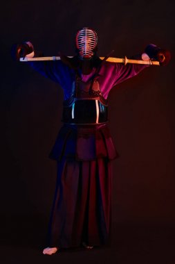 Yakın çekim, Kendo dövüşçüsü zırh giyiyor, geleneksel kimono giyiyor, miğfer takıyor shinai bambu kılıcıyla dövüş sanatları yapıyor, siyah arka plan.