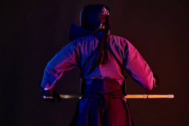 Yakından kapatın. Kendo savaşçı bir zırh giyiyor, geleneksel kimono, kask dövüş sanatı pratik, shinai bambu kılıç, geri ayakta, siyah arka plan.