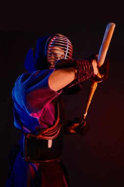 Yakın çekim, Kendo dövüşçüsü zırh giyiyor, geleneksel kimono giyiyor, miğfer takıyor shinai bambu kılıcıyla dövüş sanatları yapıyor, siyah arka plan.