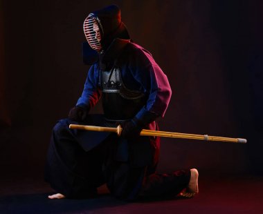 Yakın çekim, Kendo dövüşçüsü zırh giyiyor, geleneksel kimono giyiyor, miğfer takıyor shinai bambu kılıcıyla dövüş sanatları yapıyor, siyah arka plan.