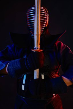 Yakın çekim, Kendo dövüşçüsü zırh giyiyor, geleneksel kimono giyiyor, miğfer takıyor shinai bambu kılıcıyla dövüş sanatları yapıyor, siyah arka plan.