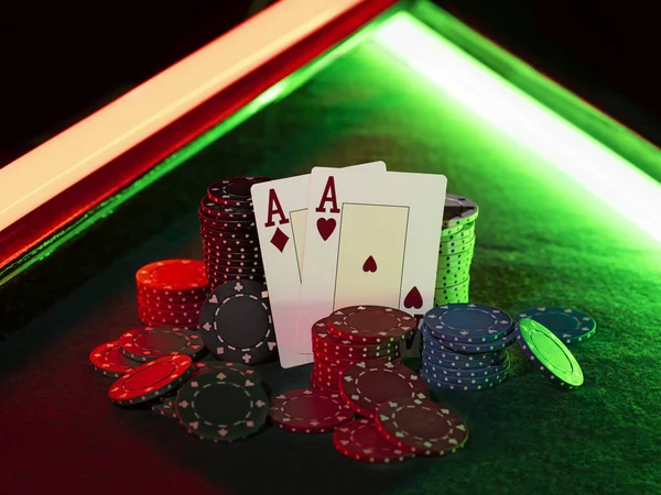 Dois ases em pé apoiados em pilhas de chips, alguns deles deitados nas proximidades na tampa verde da mesa de jogo, sob luzes de néon verde e vermelho. Close-up . — Fotografia de Stock