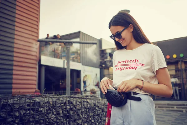 Porträt eines Mädchens mit dunkler Sonnenbrille, das in der Nähe eines Einkaufszentrums posiert. Bekleidet mit weißem T-Shirt, blauer Hose, schwarzer Taille, rotem Halstuch. — Stockfoto