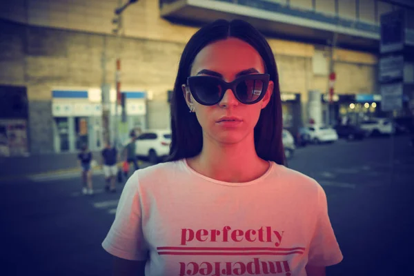 Retrato de uma menina em óculos escuros posando perto de um shopping da cidade. Vestido em t-shirt branca com a inscrição. Close-up. — Fotografia de Stock