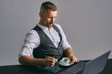 Klasik takım elbiseli, şık bıyıklı sakallı iş adamı ofiste otururken dizüstü bilgisayarda çalışıyor..